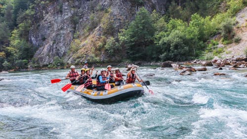 A yellow-and-white raft navigates rocky rapids in a forested mountain valley.