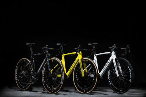 Three road bicycles—black, bright yellow, and white—are displayed side by side against a plain black background.