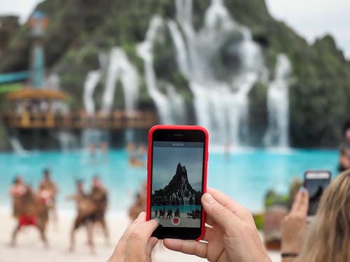 A person records a video of a themed water park attraction using a red smartphone.