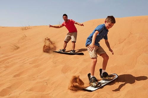 Two people ride quad bikes across a wide, open desert landscape under a pale sky.
